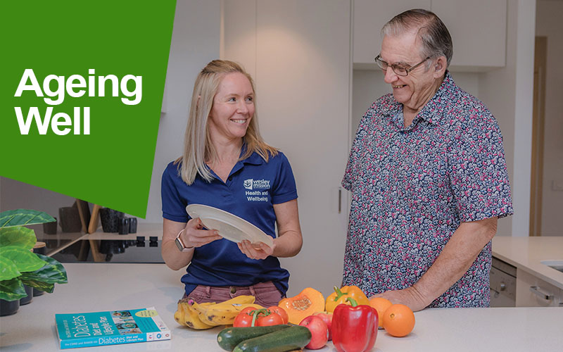 WMQ staff member in a kitchen with a aged care client with a selection of fruits and vegetables on the counter