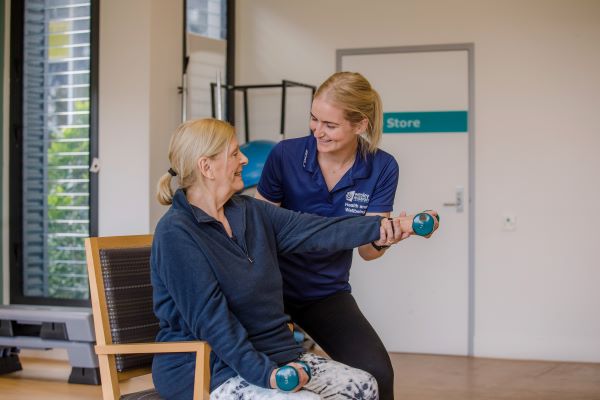Book an allied health appointment at Wesley Mission Queensland Staff helping client with dumbell as client sits in chair