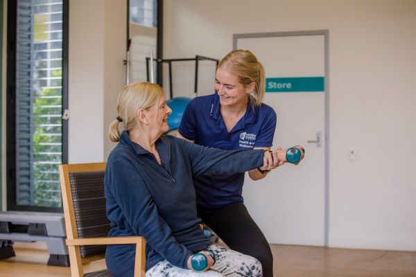 Staff helping client with dumbell as client sits in chair