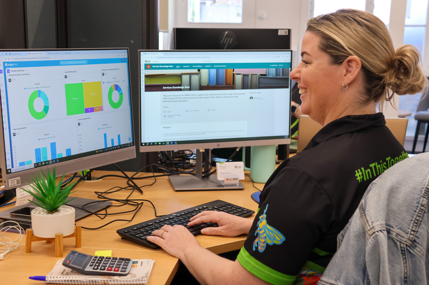 WMQ female service navigator sitting at a desk in front of two computer screens