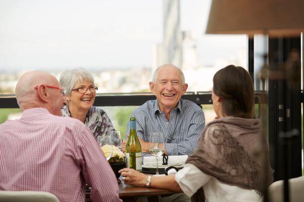 Group of retirees drinking on balcony at Aldersgate retirement village, with Brisbane's skyline in the background