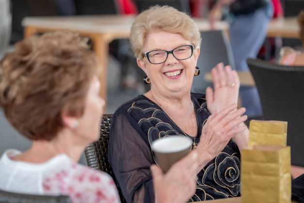 Two ladies smiling at table, one holding a drink