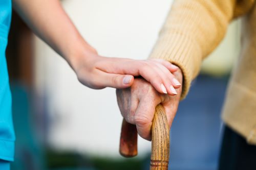 hand placed on another hand holding a walking stick