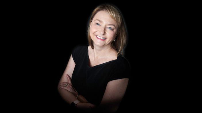 Lady stands smiling with arms crossed against black backdrop