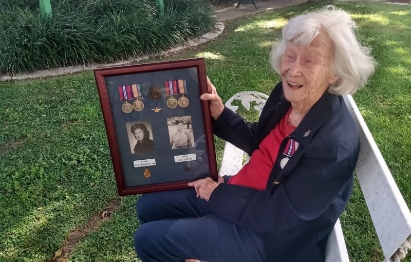 Elderly woman sitting on a park bench holding framed war memorabilia