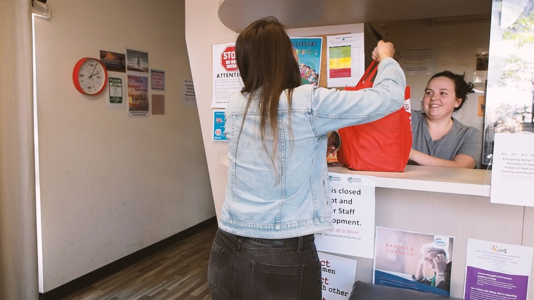 Lady accepting red grocery bag from person behind desk