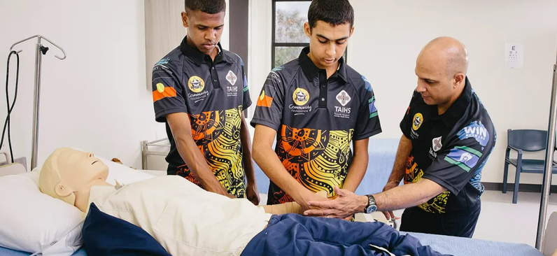 Three Indigenous men in a training exercise on a dummy on a hospital bed